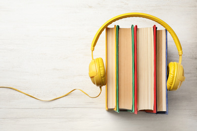 Books and modern headphones on white wooden table, top view. Space for text
