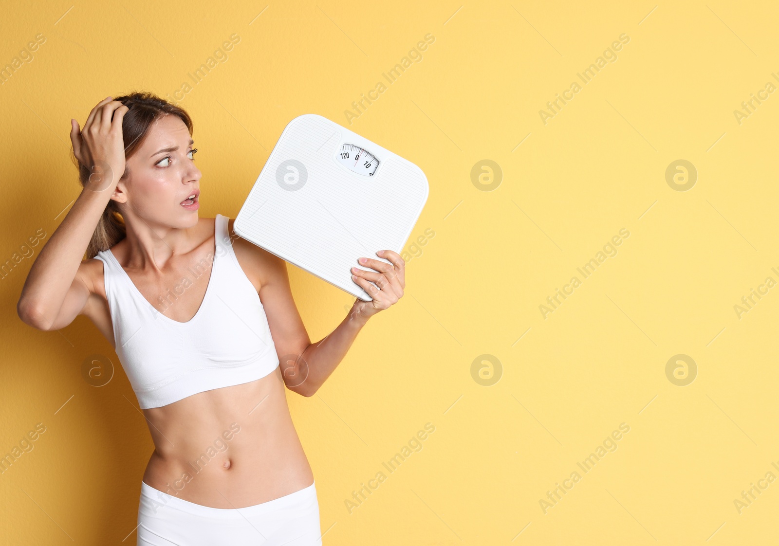 Photo of Worried young woman holding bathroom scales on color background. Weight loss diet