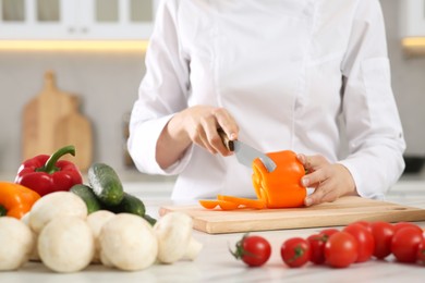 Professional chef cutting cut bell pepper at white marble table in kitchen, closeup