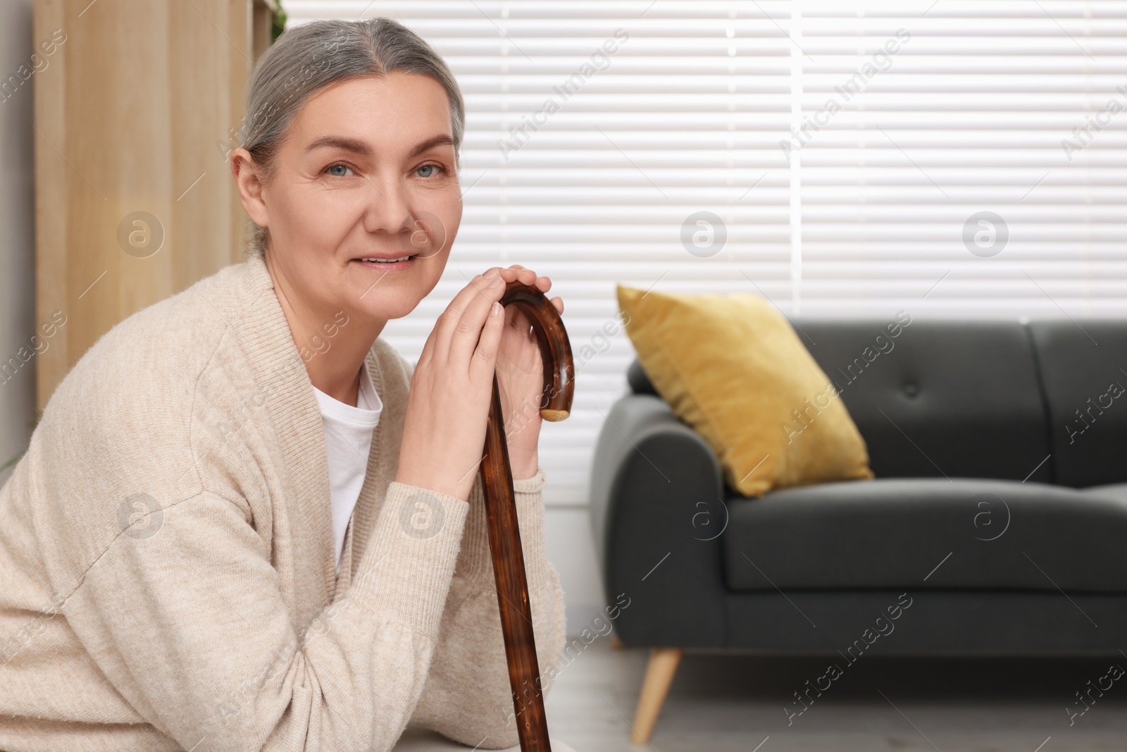 Photo of Senior woman with walking cane sitting on armchair at home. Space for text