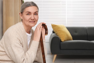 Senior woman with walking cane sitting on armchair at home. Space for text