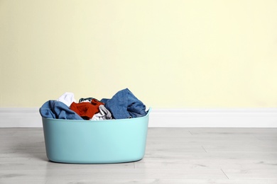 Plastic laundry basket full of dirty clothes on floor near color wall. Space for text