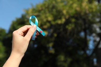 Woman holding light blue ribbon with paper blood drop outdoors, closeup. Diabetes awareness