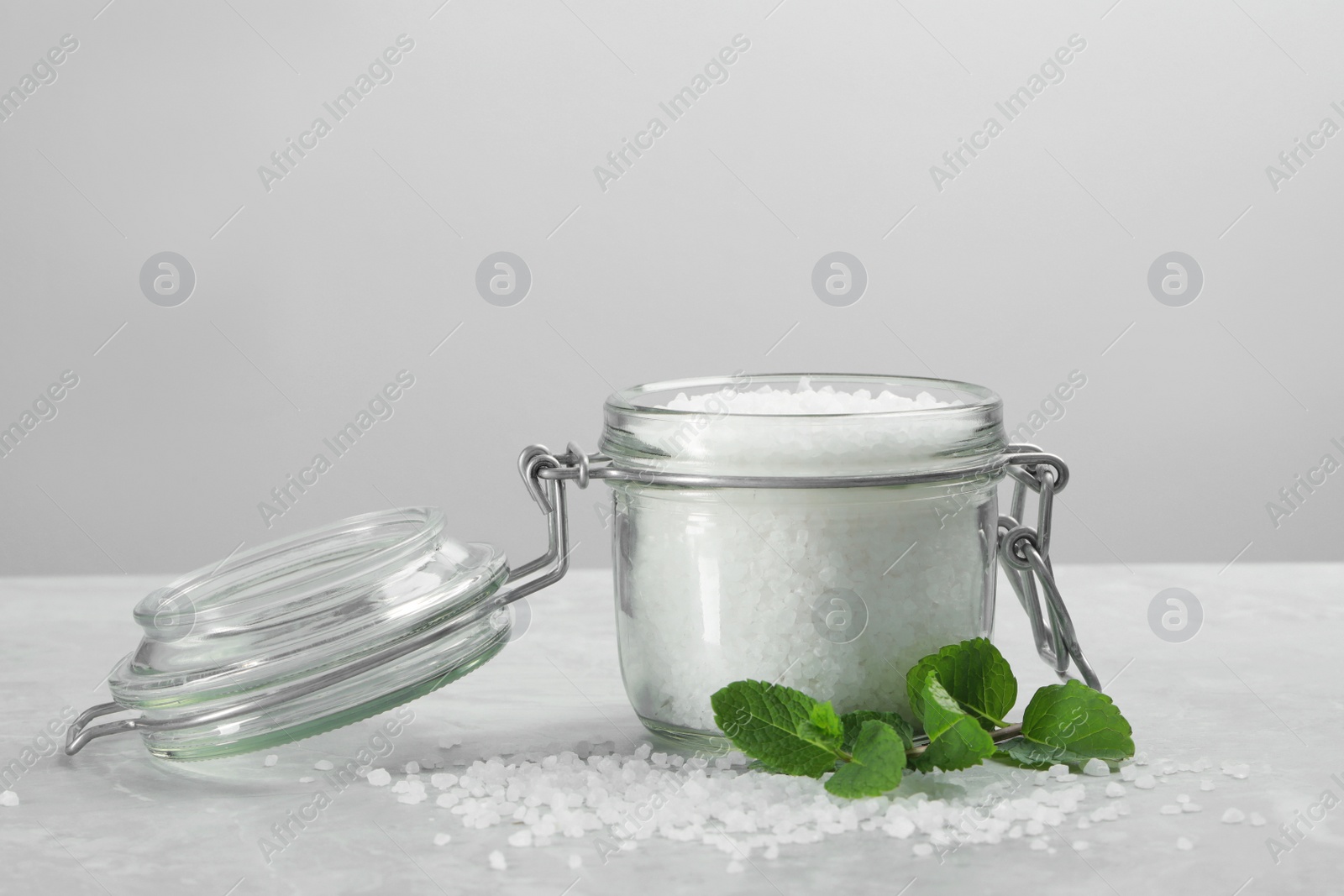 Photo of Natural sea salt in glass jar and mint on light grey marble table