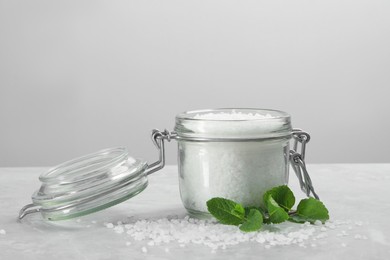 Photo of Natural sea salt in glass jar and mint on light grey marble table