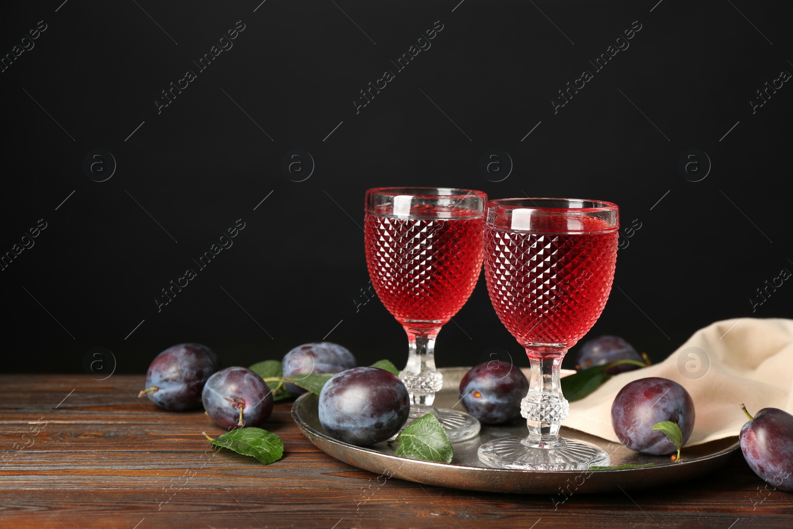 Photo of Delicious plum liquor and ripe fruits on wooden table against black background. Homemade strong alcoholic beverage