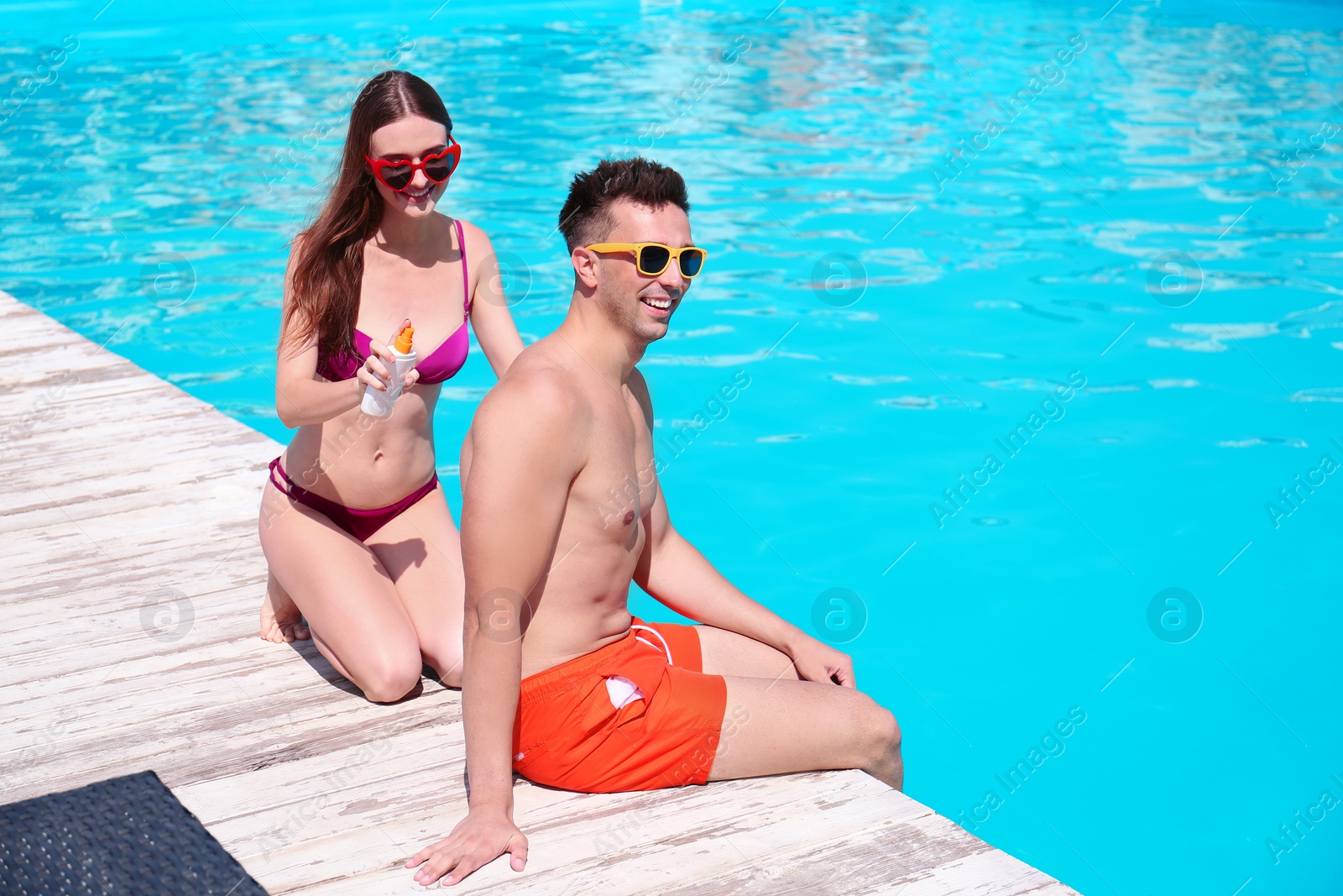 Photo of Young woman applying sun protection cream onto boyfriend at swimming pool