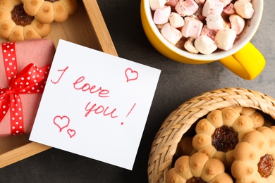 Photo of Note with phrase I love You near gift box, cookies and cup of hot drink on dark table, flat lay