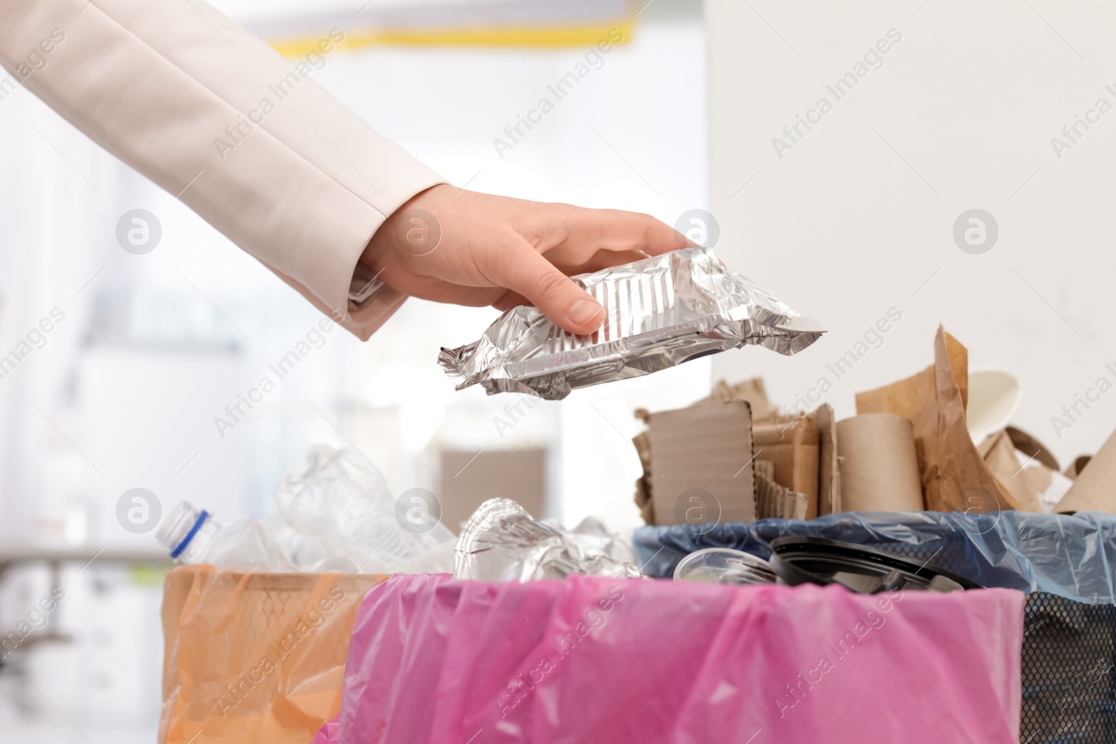 Photo of Woman putting used foil container into trash bin in office, closeup. Waste recycling