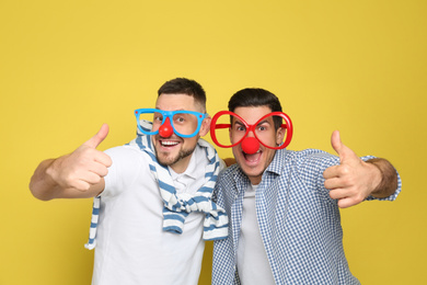 Men with funny accessories on yellow background. April fool's day