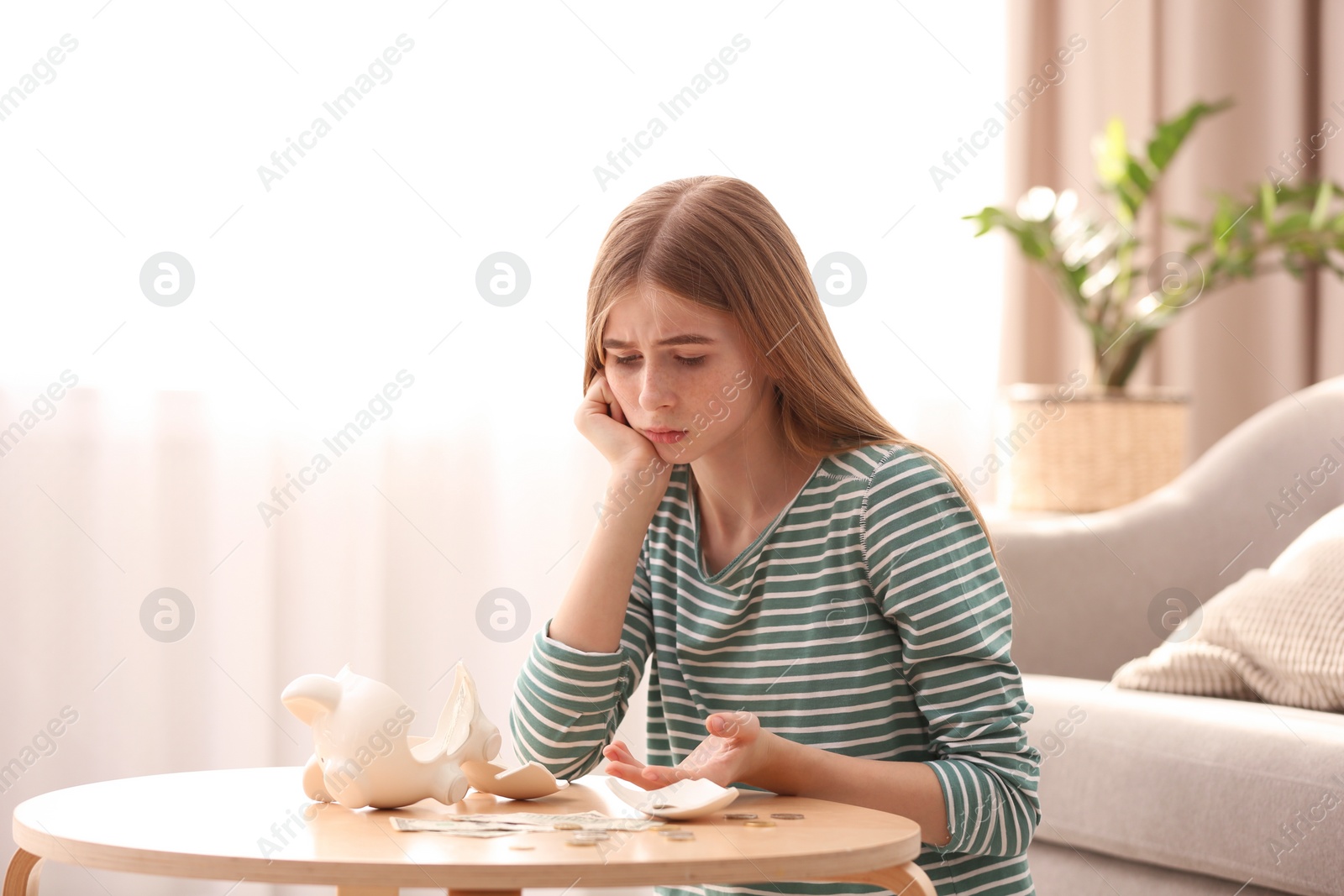 Photo of Sad teen girl with broken piggy bank and money at home