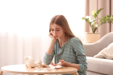 Sad teen girl with broken piggy bank and money at home