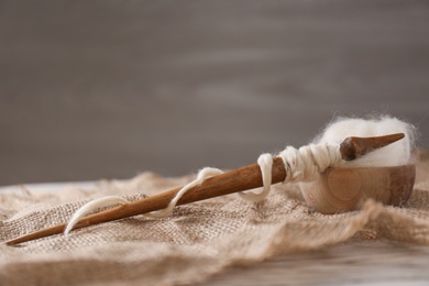 Photo of Soft white wool and spindle on table. Space for text