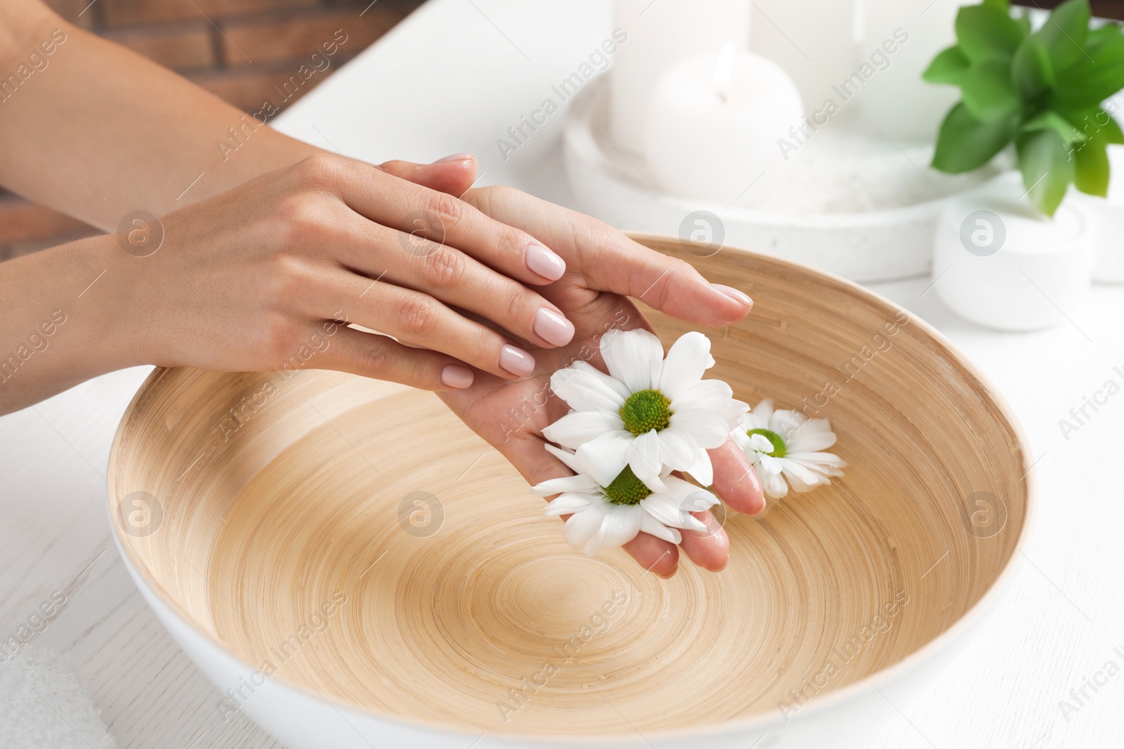 Photo of Woman soaking her hands in bowl with water and flowers on table, closeup. Spa treatment