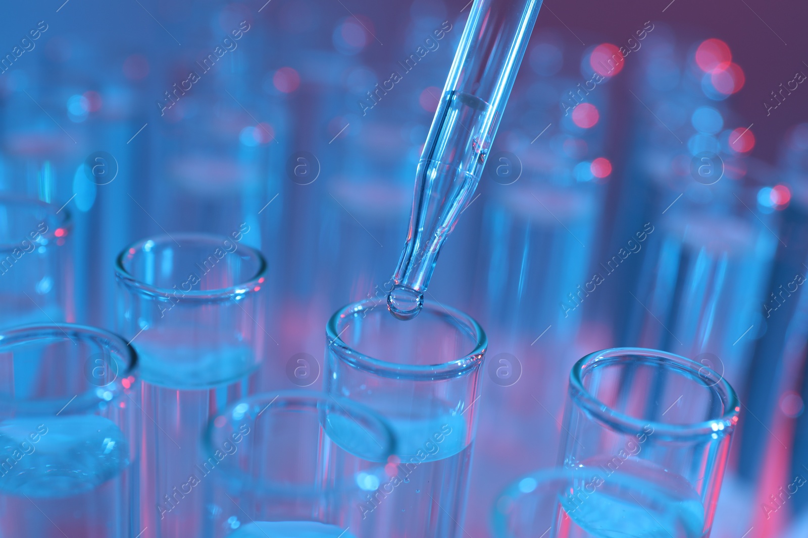 Photo of Dripping liquid from pipette into test tube on color background, closeup