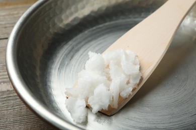 Photo of Frying pan with coconut oil and wooden spatula on wooden table, closeup. Healthy cooking