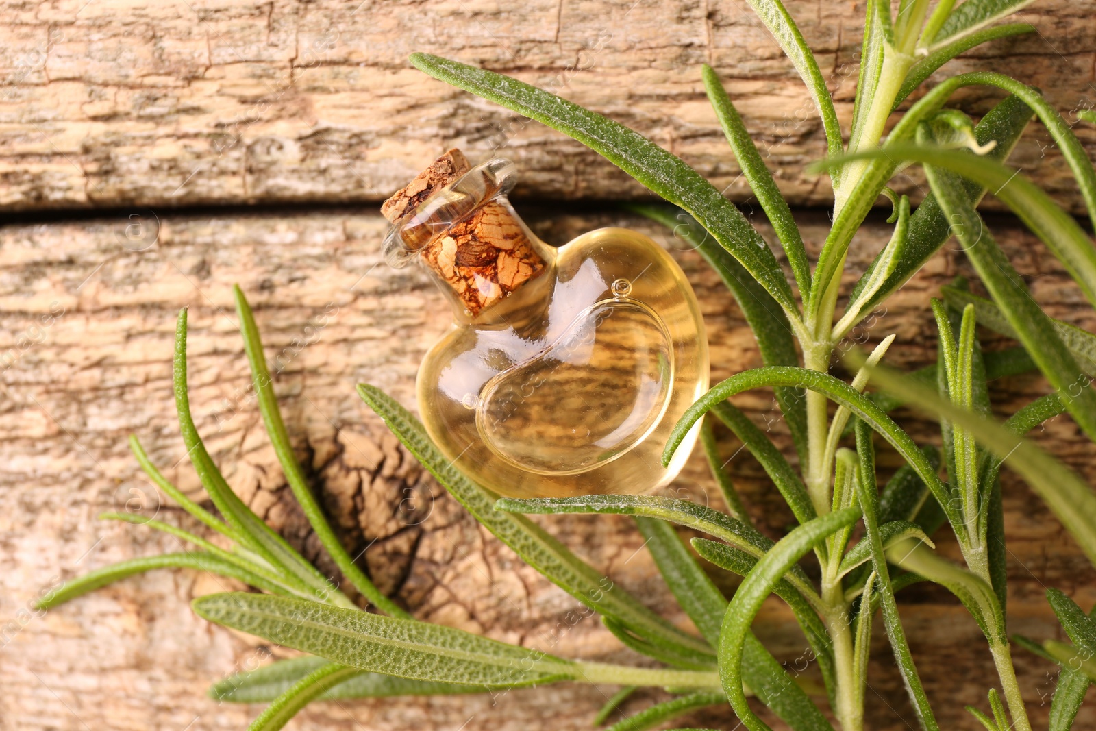 Photo of Aromatic essential oil in bottle and rosemary on wooden table, flat lay