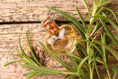 Photo of Aromatic essential oil in bottle and rosemary on wooden table, flat lay