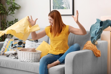 Photo of Tired and annoyed housewife throwing clothes at home