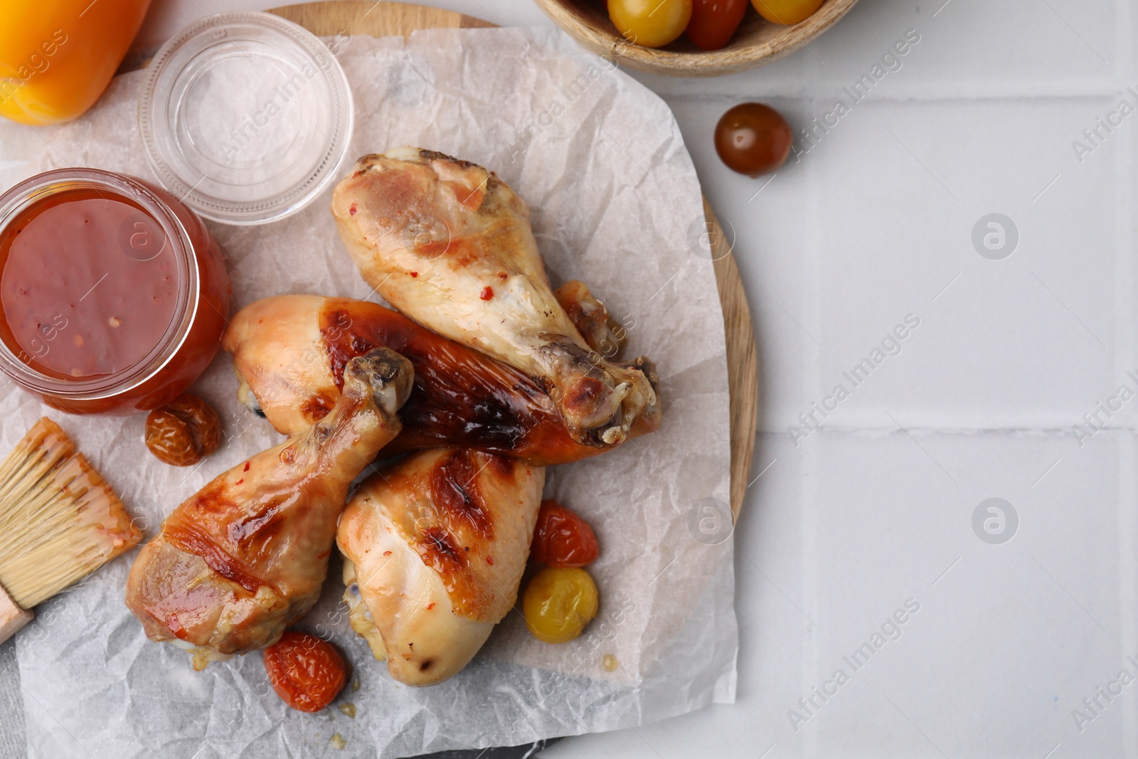 Photo of Marinade, basting brush, roasted chicken drumsticks and tomatoes on white tiled table, flat lay. Space for text