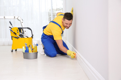 Photo of Professional janitor cleaning baseboard with brush after renovation
