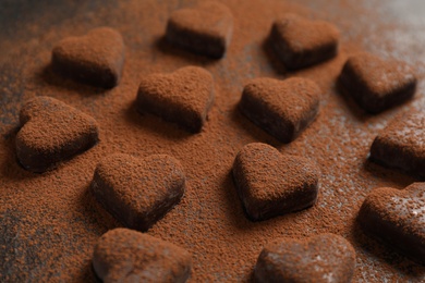 Photo of Beautiful heart shaped chocolate candies with cocoa powder on black table, closeup
