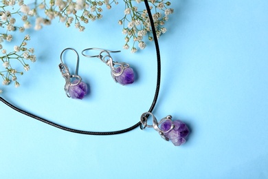 Photo of Beautiful silver necklace and pair of earrings with amethyst gemstones on light blue background