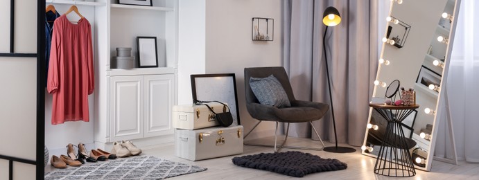 Makeup room. Stylish mirror with light bulbs, beauty products on side table and armchair indoors, banner design