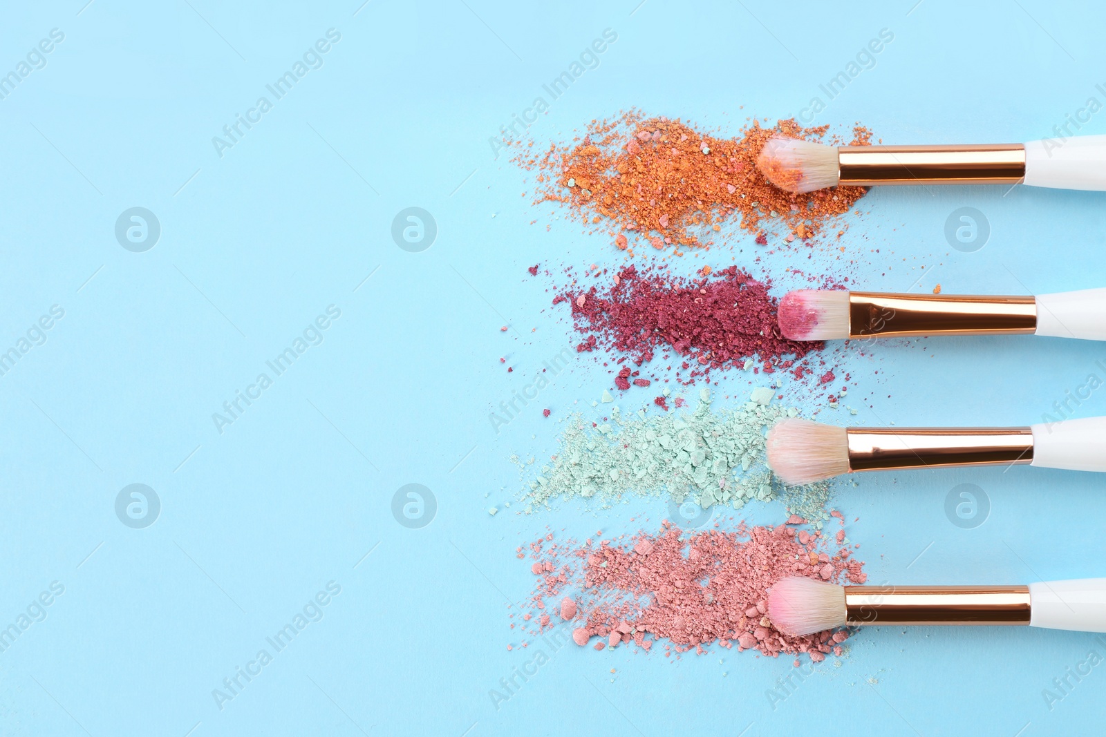 Photo of Makeup brushes and scattered eye shadows on light blue background, flat lay. Space for text