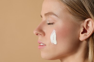 Photo of Beautiful young woman with sun protection cream on her face against beige background, closeup. Space for text