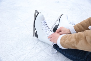 Photo of Woman lacing figure skate while sitting on ice rink, closeup