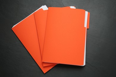 Orange files with documents on black slate table, top view