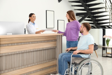 Photo of Professional receptionist working with woman and handicapped man at desk in clinic
