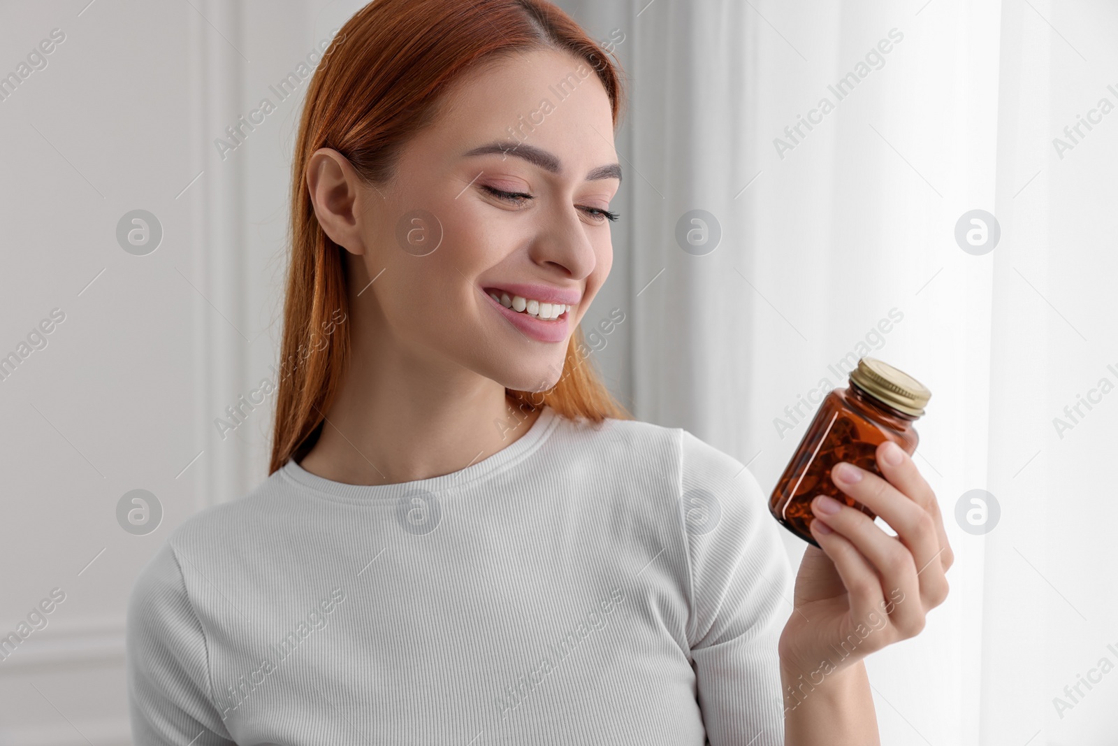 Photo of Beautiful young woman with jar of vitamin pills at home