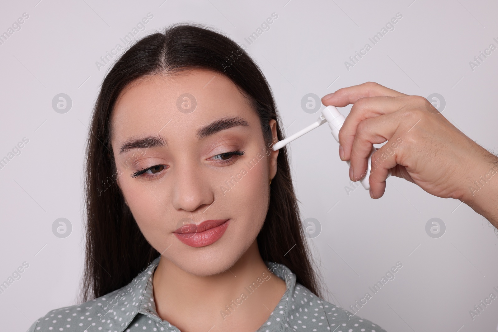 Photo of Senior man spraying medication into woman's ear on white background