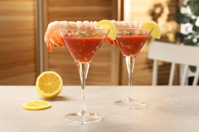 Tasty shrimp cocktail with sauce in glasses and lemon on light marble table