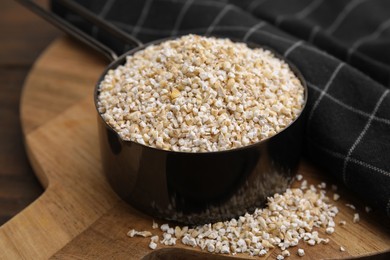Photo of Raw barley groats in scoop on wooden table, closeup