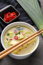 Photo of Bowl of delicious miso soup with tofu and chopsticks served on grey table