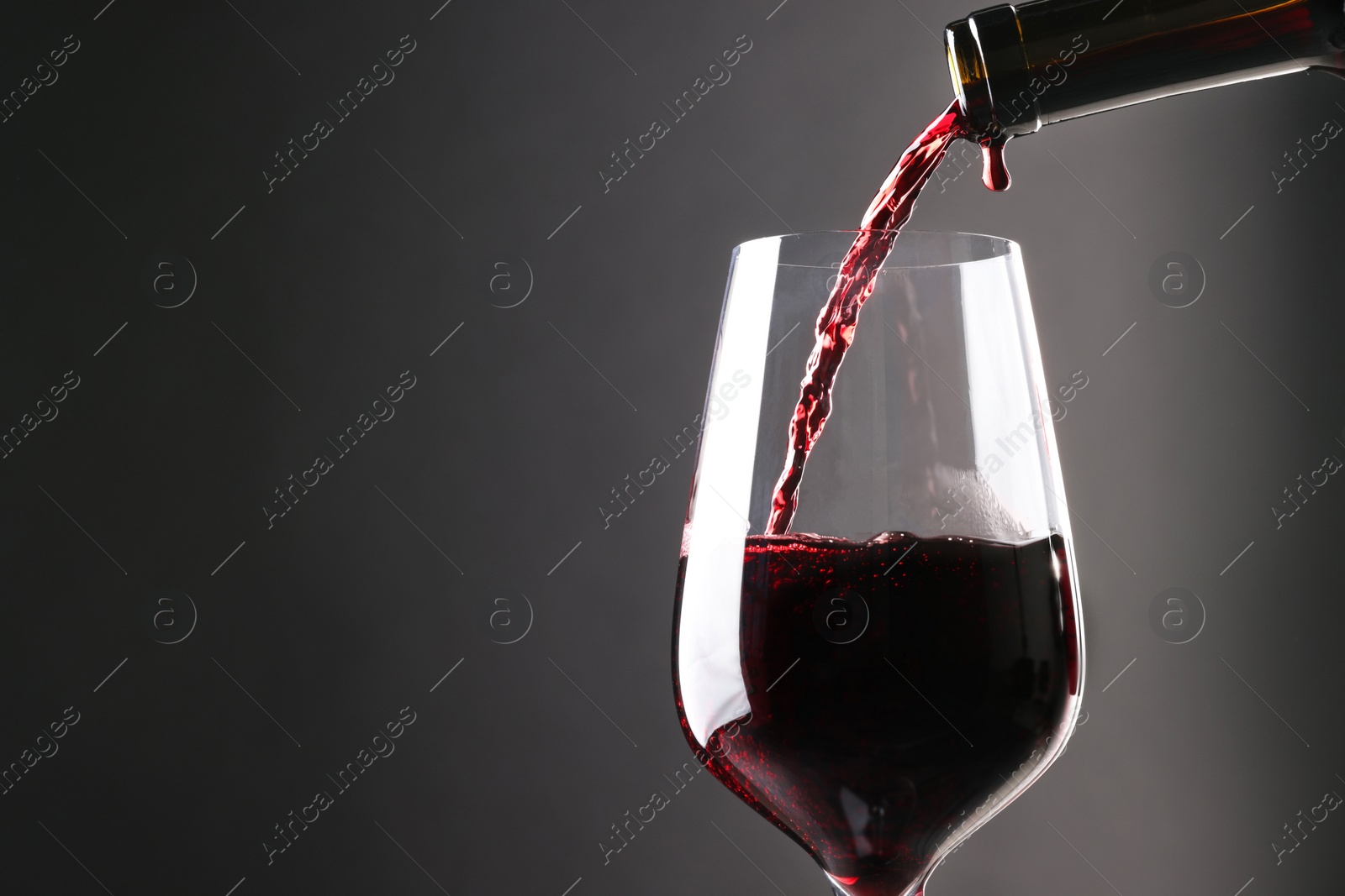 Photo of Pouring red wine into glass against grey background, closeup. Space for text