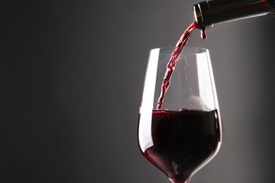 Photo of Pouring red wine into glass against grey background, closeup. Space for text