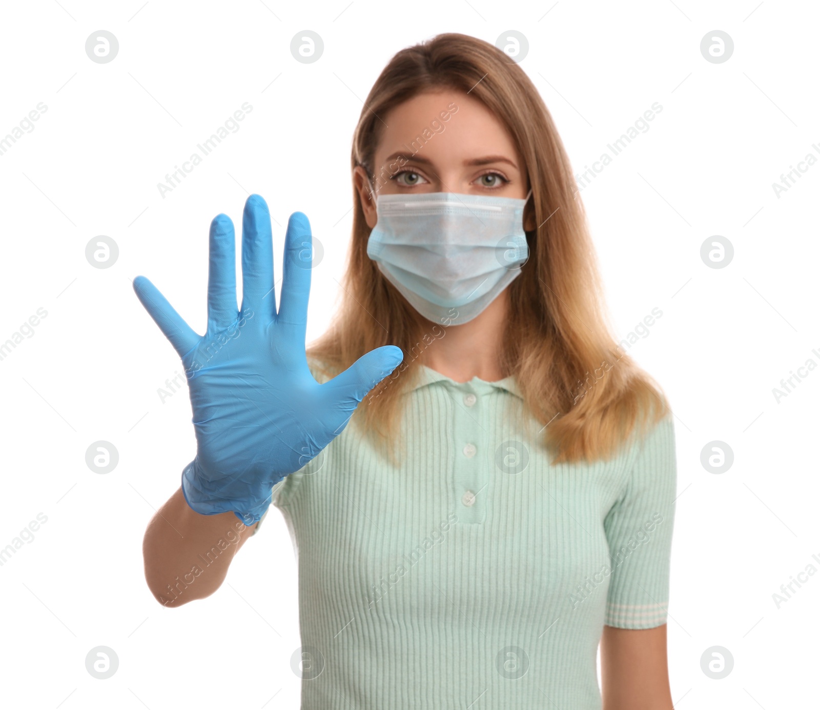 Photo of Young woman in medical gloves and protective face mask showing stop gesture against white background, focus on hand