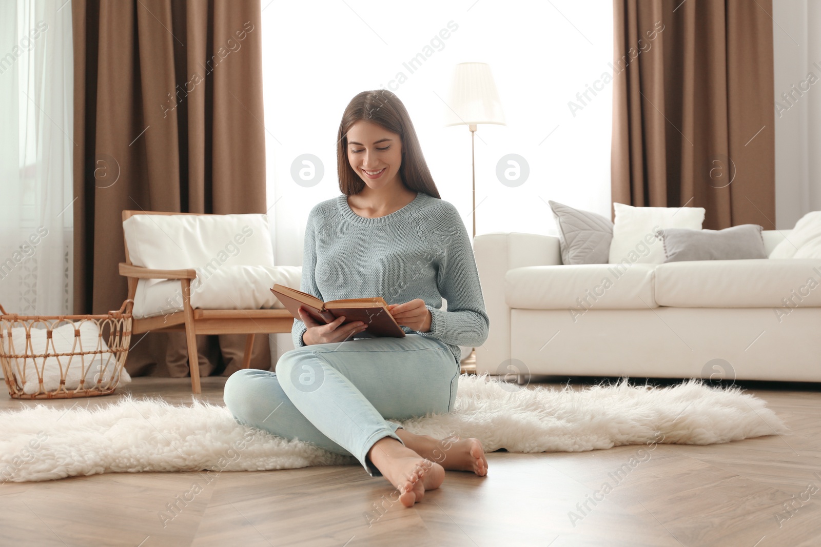 Photo of Beautiful young woman reading book at home. Floor heating concept