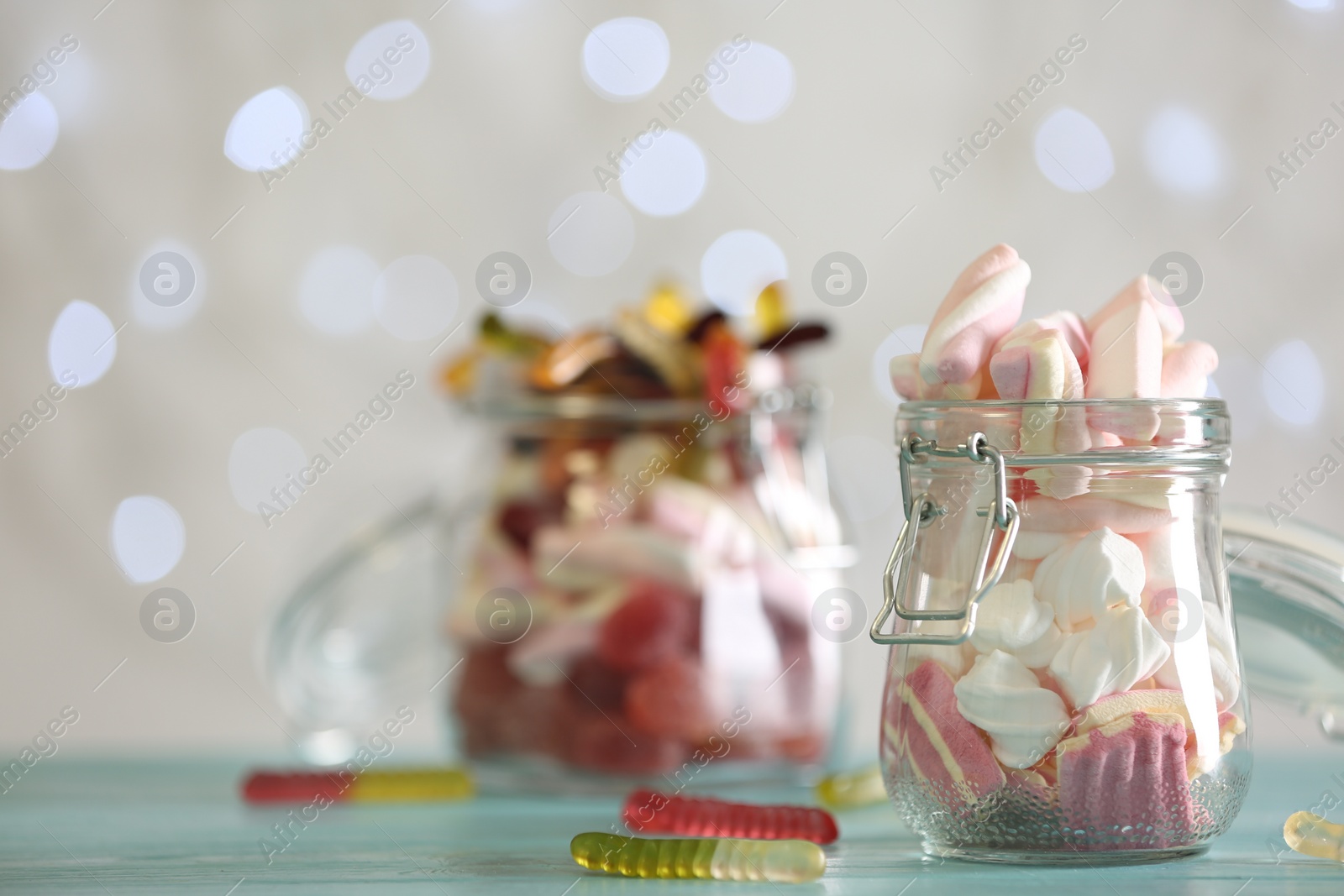Photo of Delicious marshmallows in jar on table against blurred background, closeup. Space for text