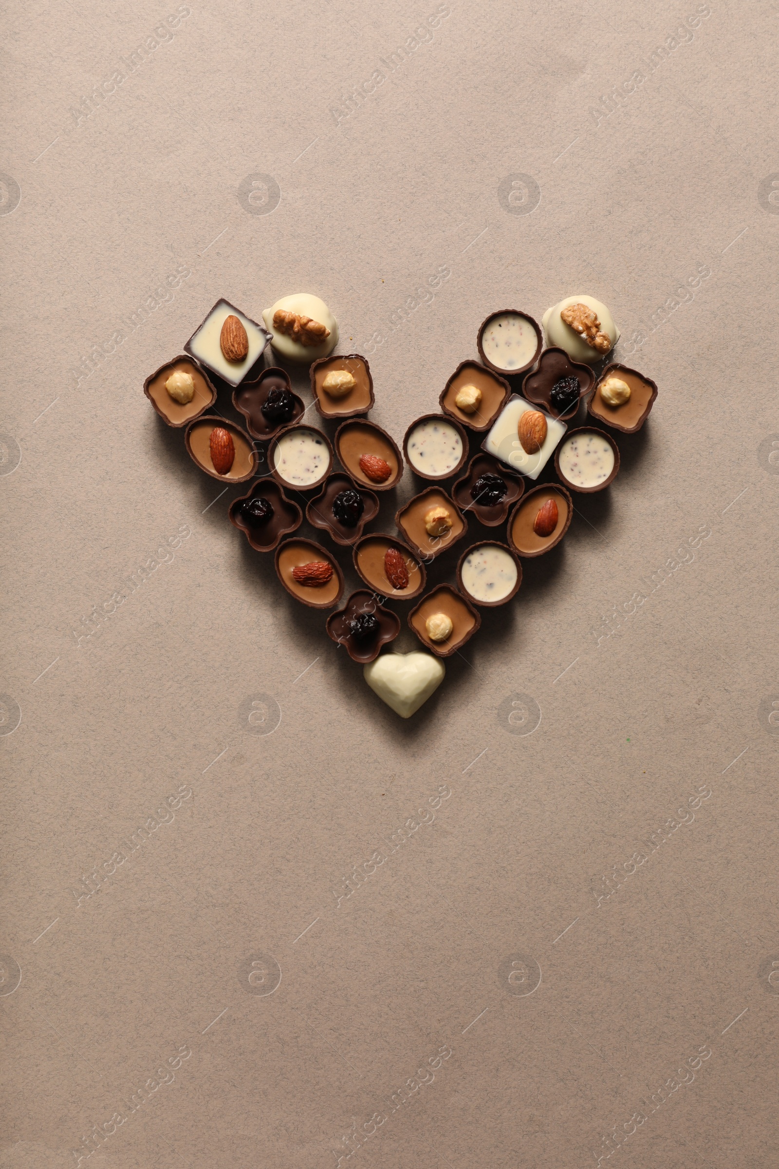 Photo of Heart made with delicious chocolate candies on beige background, top view