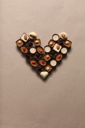 Heart made with delicious chocolate candies on beige background, top view