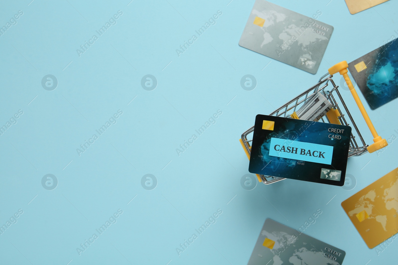Photo of Credit cards and dollar banknotes in shopping cart on light blue background, flat lay with space for text. Cashback concept