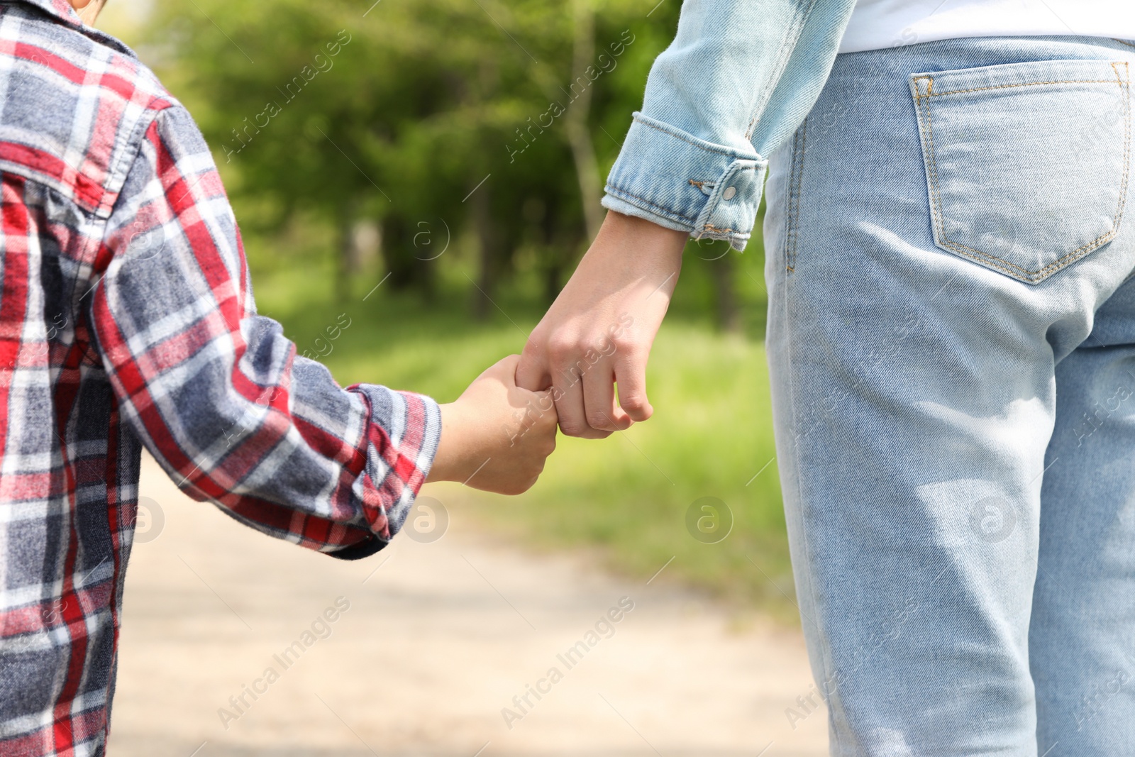 Photo of Little child holding hands with his mother outdoors, closeup. Family time