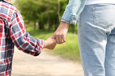 Little child holding hands with his mother outdoors, closeup. Family time