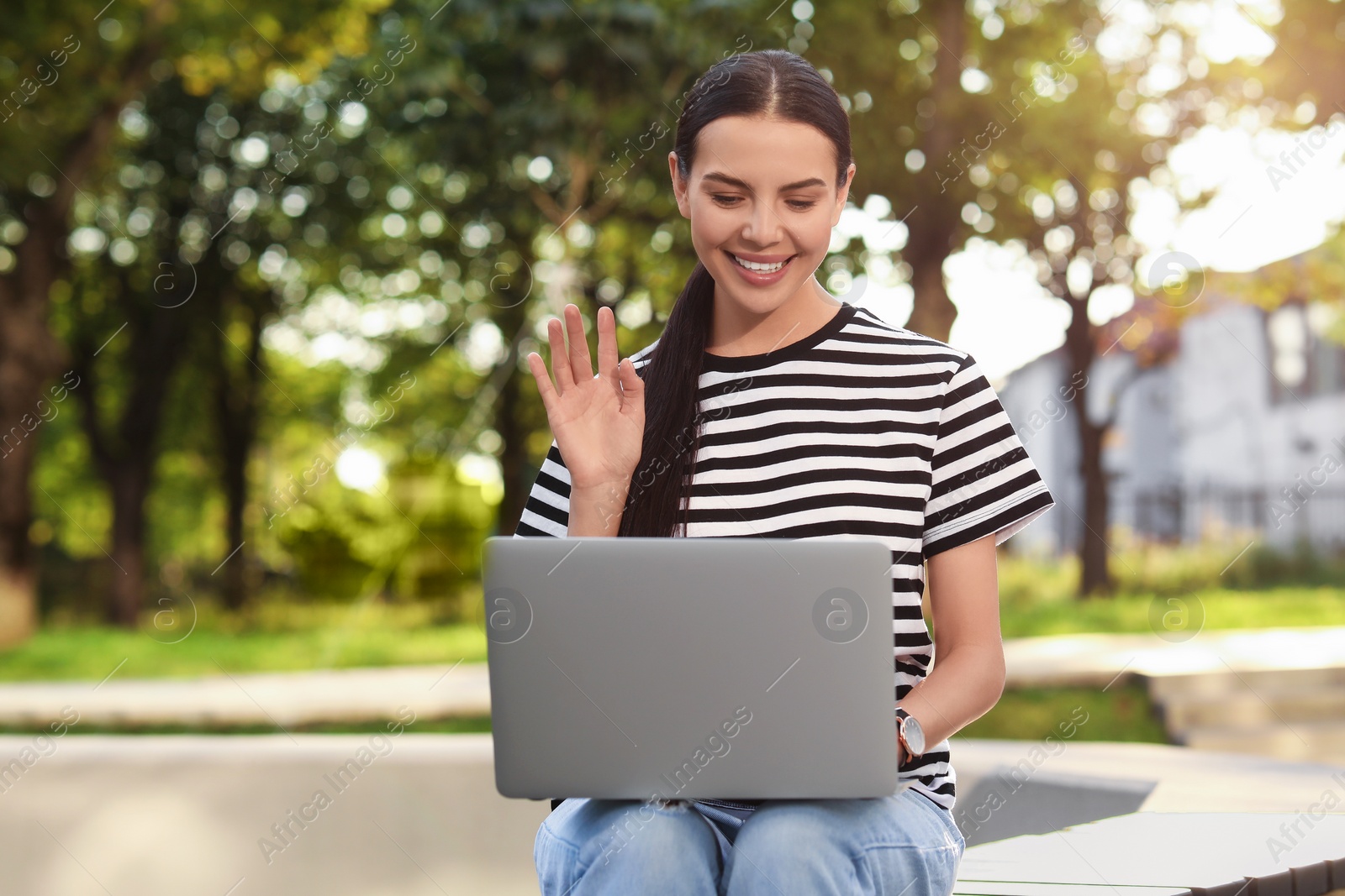 Photo of Happy young woman using modern laptop for video call outdoors