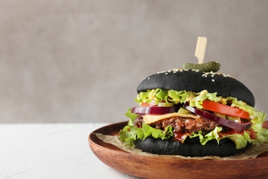 Wooden plate with black burger on table, space for text